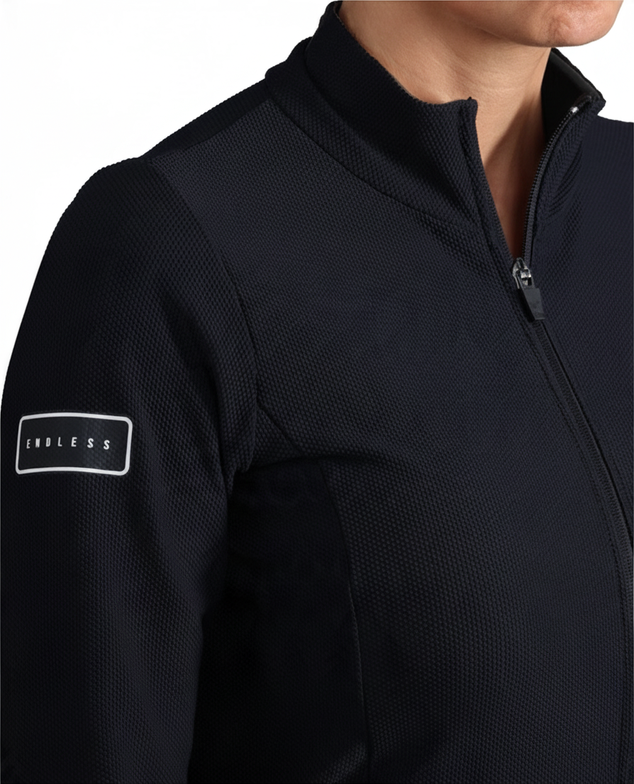 Chaqueta deportiva negra Endless para mujer con cuello alto, cremallera frontal y logo en la manga.