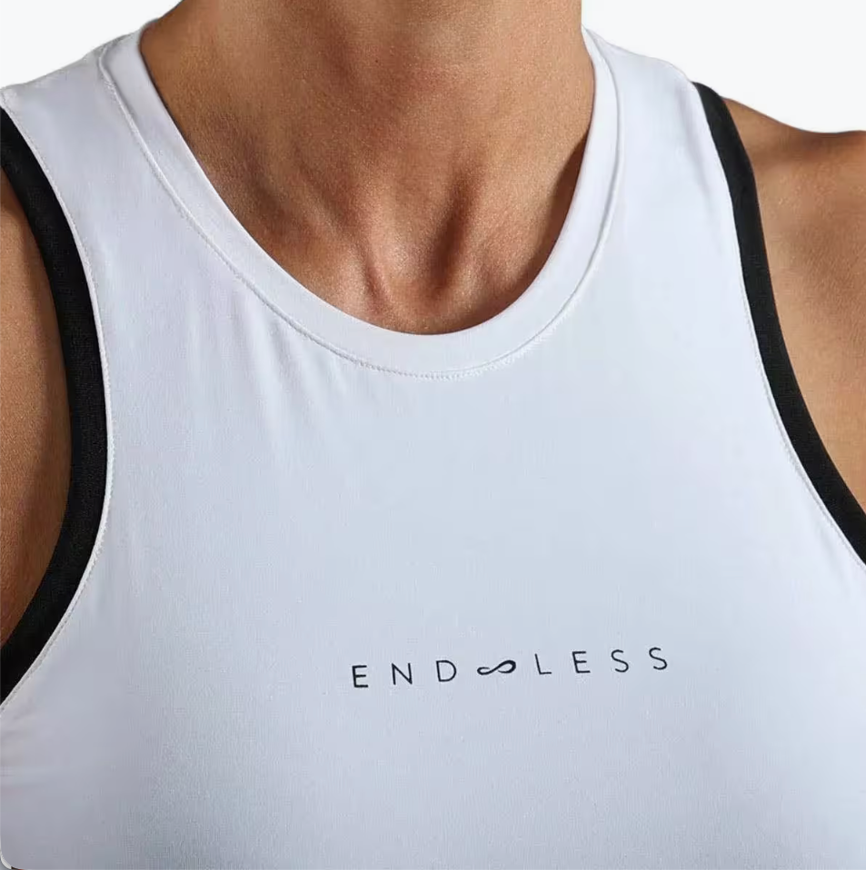 Top deportivo Endless MX blanco con cuello cerrado y detalles en contraste negro para tenis y pádel.
